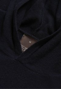 Pull en maille noir avec col en V et étiquette de vêtement de taille moyenne partiellement visible à l'intérieur.