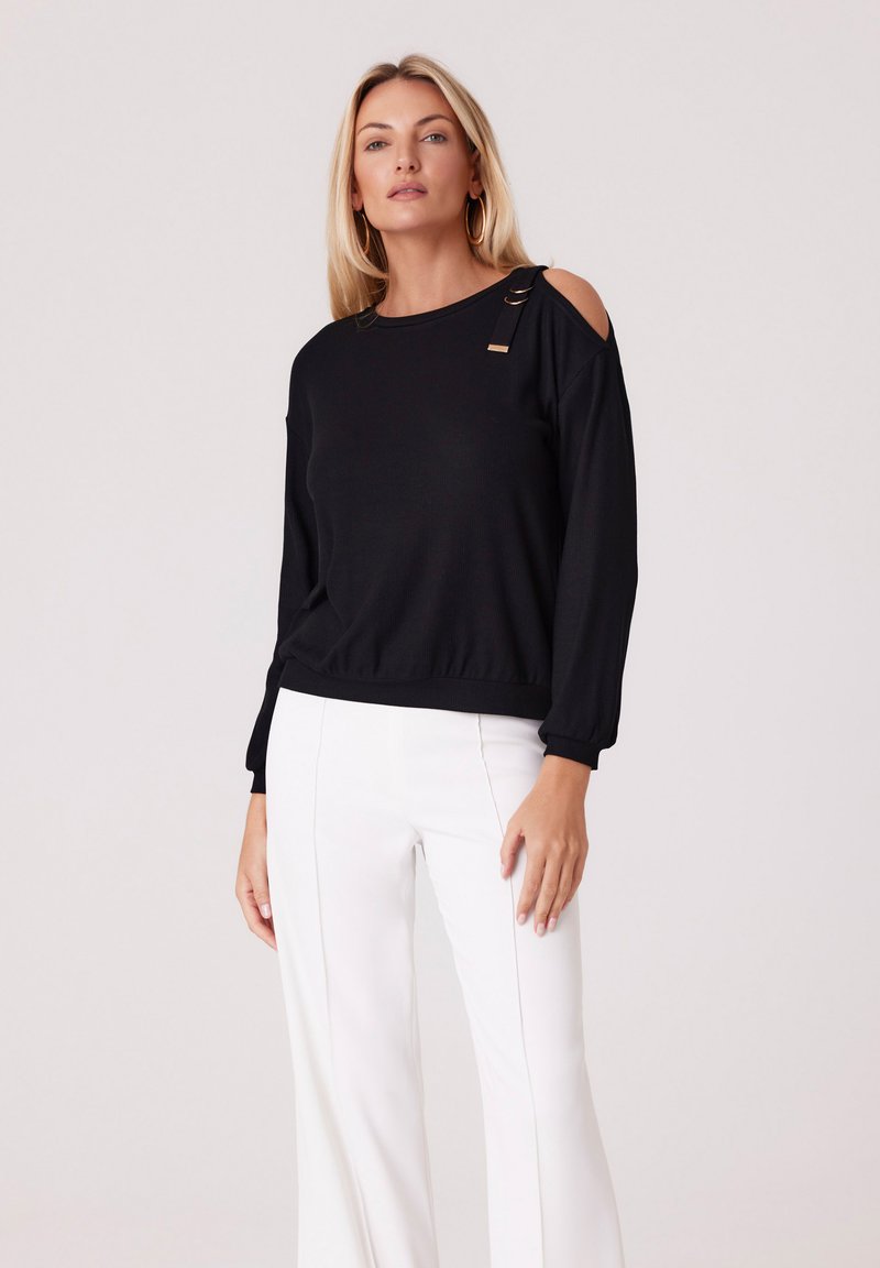 Czarny top z długim rękawem w fasonie typu cold shoulder, z złotymi akcentami i prążkowaną teksturą, zestawiony z białymi spodniami o szerokich nogawkach.