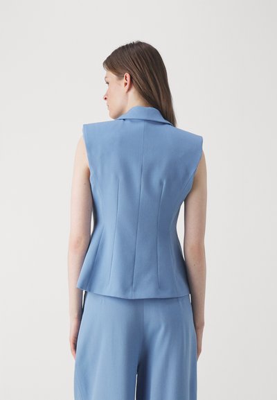 Svetlo modri brezrokavnik s kragnom, strukturiranim ramenskim dizajnom in razširjenim peplum robom. Gladek material z vertikalnimi šivi.