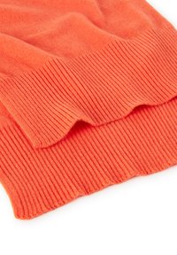 Maglione arancione lavorato a maglia con una texture liscia, caratterizzato da un orlo a coste e dettagli laterali. Il tessuto appare morbido e leggero.