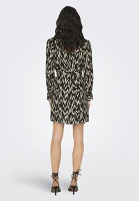 Μικρό φόρεμα με αφηρημένο μαύρο και μπεζ ζιγκ ζαγκ σχέδιο, διαθέτει μακρύτερα μανίκια, ζωνάκι στη μέση και ψηλοτάκουνα σανδάλια με λουράκια.