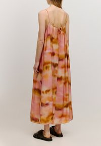 Maxi-jurk van roze en bruine tie-dye stof, met dunne spaghettibandjes en een geplooide achterkant. Gecombineerd met zwarte instapsandalen.