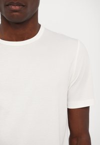 Short-sleeved white t-shirt with a round neckline, made of smooth fabric, featuring a subtle texture and minimal design.