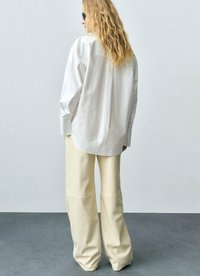 Witte oversized blouse met lange mouwen, gecombineerd met crèmekleurige wijde broekspijpen. Zachte stoftextuur, minimalistisch ontwerp.