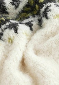 Écharpe en tissu tricoté avec une texture moelleuse blanche, ornée d'accents vert foncé et noir, mettant en valeur des motifs complexes et une grande douceur.