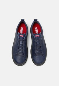 Navy lädersneakers med perforerade detaljer, svart gummisula och röd innersula med "CAMPER"-logotyp på hälen och tungan.