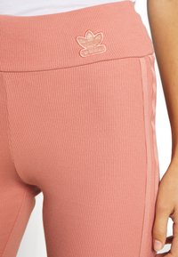 Leggings rosa a coste con vita alta, dotati di un logo ricamato in oro e dettagli laterali per un aspetto testurizzato e aderente.