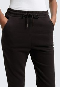 Schwarze, lässige Sweatpants mit einem Kordelzugbund, seitlichen Taschen und einer glatten Textur.