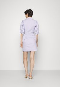 Vestido curto lilás claro com mangas bufantes, cintura cingida e corte reto. O tecido parece macio, com detalhes mínimos.