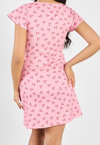 Lyhyt vaaleanpunainen mekko, jossa on levenevät hihat ja toistuva kirsikkakuosi. Valmistettu ribbitetusta kankaasta, sillä on istuva siluetti ja sivuaukot.