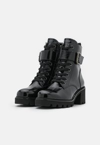Des bottines en cuir verni noir présentent un talon épais, un laçage à l'avant, et un détail de bride à boucle. La semelle est dotée d'un design texturé et robuste.