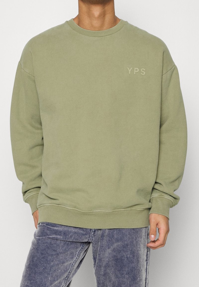 Olivově zelená mikina s kulatým výstřihem, žebrovanými manžetami a spodním lemem, s jemným logem YPS na hrudi. Měkký materiál a volný střih.
