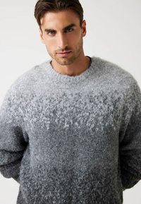 Maglione grigio con un design a gradiente che passa dal grigio chiaro al grigio scuro, realizzato in un materiale morbido e texture, con scollo rotondo e maniche lunghe.