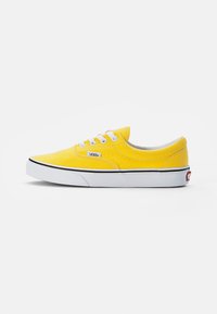 Gul lærrete sneaker med hvite snørebånd, hvit gummisåle og svarte detaljer. Har et Vans-logo på siden. Klassisk low-top design.