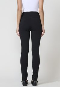Črne legice z visokim pasom, gladko teksturo, slim fit obliko, ki se zožuje pri gležnjih. Utekane z oprijetim belim vrhom in črnimi čevlji.