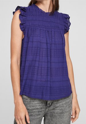 Fialová halenka bez rukávů s volánkovými rameny a texturovanými vodorovnými pruhy, kombinovaná s šedými vypranými džíny na stojící osobě.