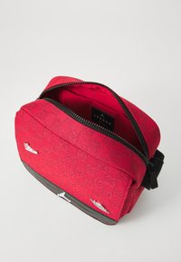 Borsa a spalla rossa in tessuto con superficie texture e fondo nero. Presenta una chiusura con zip, una tasca interna e piccoli dettagli con logo.