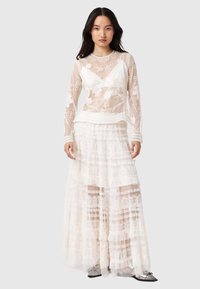 Weißes Schichtkleid mit transparenter, floral bestickter Langarmbluse und gestuftem Spitzenrock, der Rüschen und strukturierte Details aufweist.