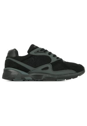 Zapatillas deportivas negras con parte superior de ante y malla, acentos grises, diseño de cordones y suela texturizada. Logo dinámico en el lateral.