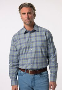 Camicia a maniche lunghe con motivo plaid blu e giallo, caratterizzata da un colletto abbottonato, tessuto morbido e vestibilità rilassata. Abbinata a jeans azzurri chiari.