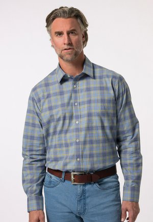 Camisa de manga larga en patrón de cuadros azul y amarillo, con cuello abotonado, tejido suave y un corte relajado. Combinada con jeans de mezclilla azul claro.