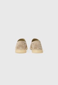Beige Wildleder-Loafers mit einer glatten Textur, runder Zehenpartie und einer niedrigen Gummisohle. Sichtbare Steppnähte auf der Rückseite.