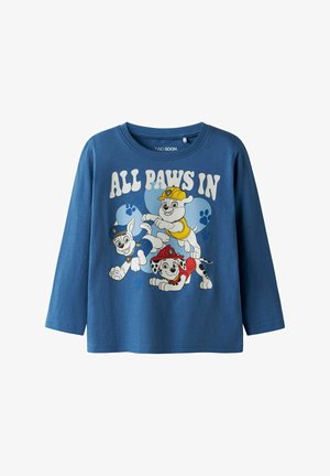 Garšīgas piedurknes zila kokvilnas T-krekls ar animētiem suņiem krāsainos apģērbos. Uzraksts "VISAS ĶEPAS IEKŠĀ" ar ķepu nospiedumu akcentiem.