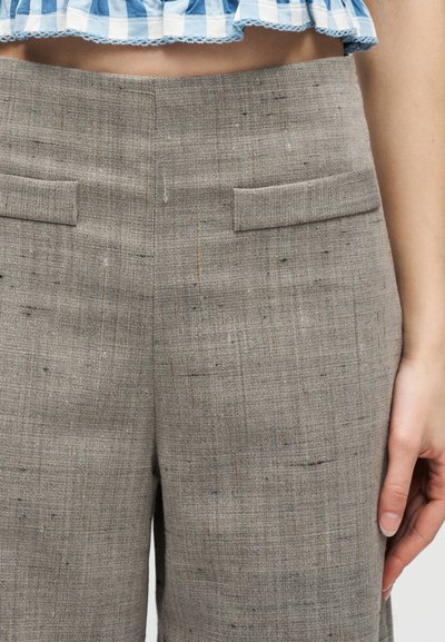 Γυναίκα που φοράει ψηλόμεσο γκρι υφασμάτινο παντελόνι με τσέπες με καπάκι, σε συνδυασμό με κοντό μπλε και λευκό καρό τοπ.