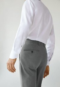 Witte lange mouwen shirt met knoopmanchetten en lichtgrijze broek met een achterzak. Het gladde materiaal en de op maat gemaakte pasvorm zijn zichtbaar.