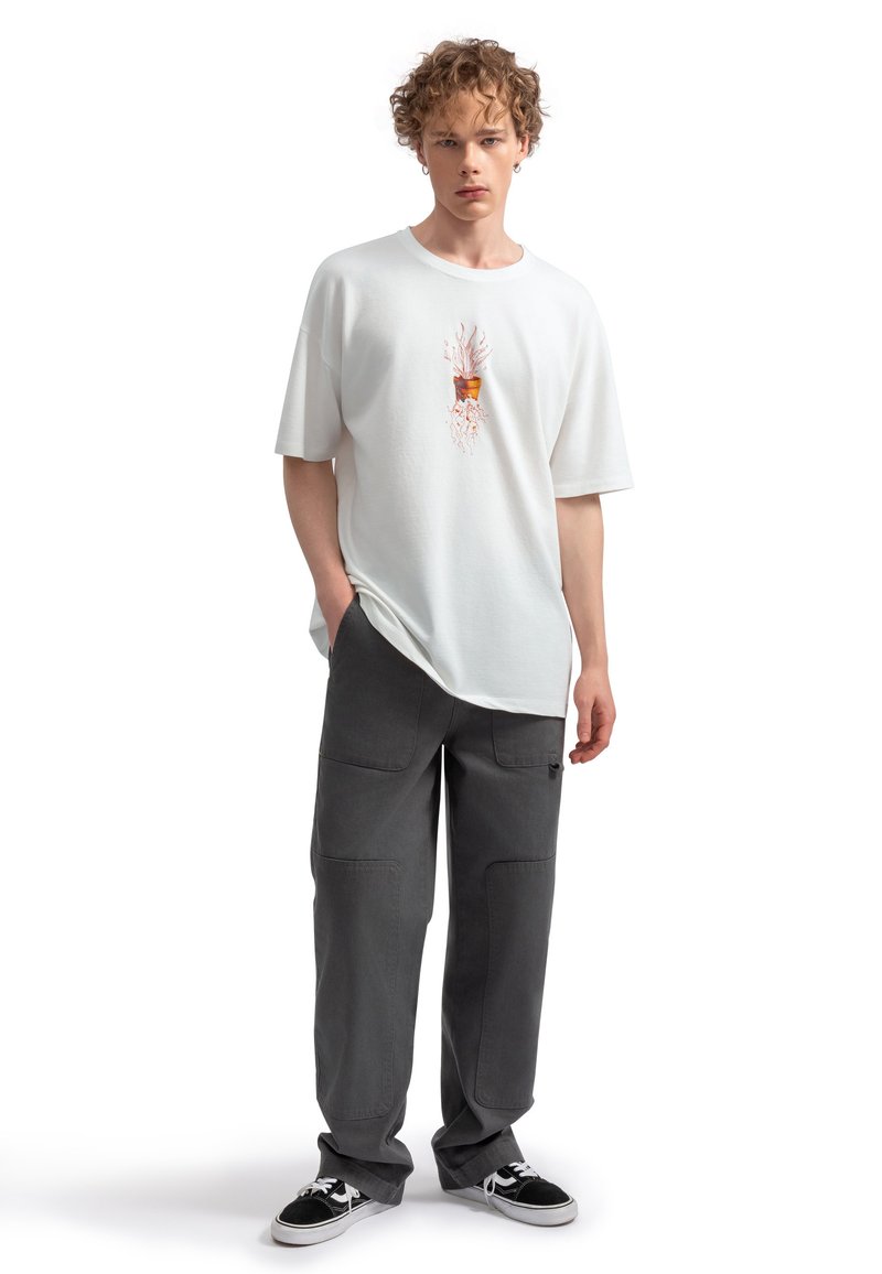 Witte katoenen t-shirt met een plantgrafiek, gecombineerd met loszittende grijze cargobroeken met meerdere zakken en stiksels.