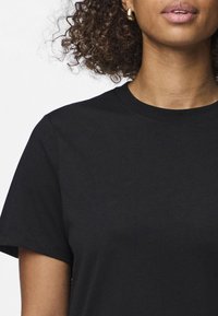 Juodas medvilnės marškinėliai su apvaliu kaklu ir trumpomis rankovėmis. Audinys atrodo lygus, su klasikiniu kirpimu ir minimaliu siuvimo detalių kiekiu.