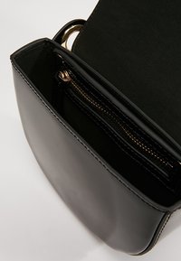Černá kožená taška s hladkým povrchem, uvnitř s kapsou na zip. Zaoblené hrany a zlaté kovové detaily.