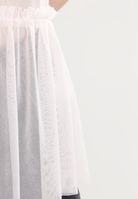 Světle růžový tylový top s řaseným výstřihem a přiléhavým pasem. Průhledný, lehký materiál s jemnou texturou.