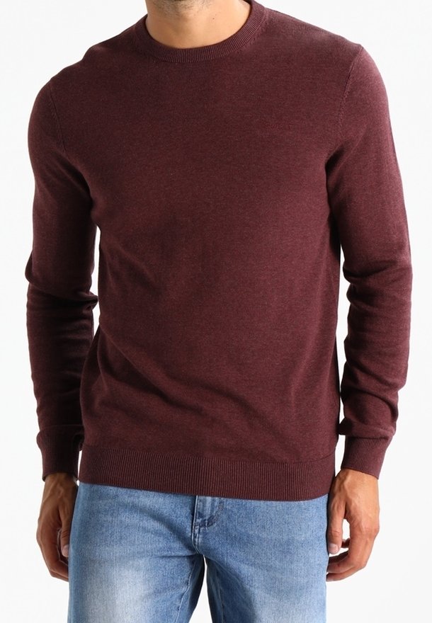 Burgunderfarbener Rundhalsausschnitt-Pullover aus weichem Strickstoff. Lange Ärmel mit gerippten Bündchen und Saum, kombiniert mit hellblauen Jeans.