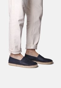 Marinblå läderespadriller med jutesula, slips-on design och kontrasterande sömmar. Bärs med uppvikta ljusa byxor.