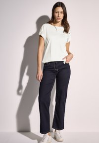 Camiseta blanca de manga corta, un corte relajado, combinada con jeans de pierna recta de color azul oscuro y zapatillas blancas. Diseño simple con hardware mínimo.