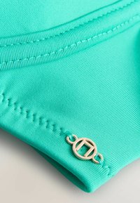 Turkizen modro kopalniško blago z gladko teksturo, ojačanim šivanjem in poudarkom iz zlatih kovinskih detajlov.