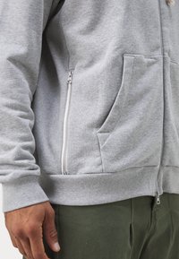 Sivá mikina na zips vyrobená z mäkkého fleesu, so bočnými vreckami, rebrovanými manžetami a hladkým povrchom s detailom kovového zipsu.