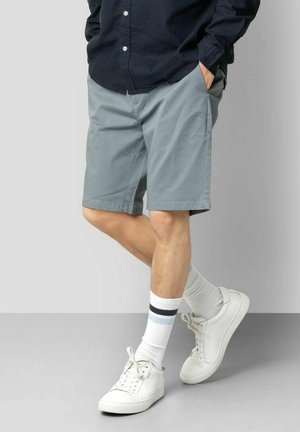Grå shorts med en afslappet pasform, lavet af letvægtsstof, med sidelommer og lige kant. Paret med hvide sneakers og stribede sokker.