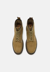 Stivali ankle in suede marrone con punta arrotondata, lacci beige e cuciture gialle a contrasto. Presentano un pratico pomo sul tallone e un interno texturizzato.