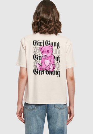 Kremfarget oversized t-skjorte med et rosa bamsetrykk med en sydd smil og "Girl Gang"-tekst i svart på baksiden.