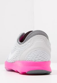 Harmaat lenkkarit, joissa on teksturoidusta verkkokankaasta valmistettu yläosa ja vaaleanpunainen kumipohja. Varustettu valkoisella swoosh-logolla ja pehmustetulla harmaalla kauluksella mukavuutta varten.