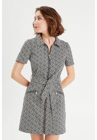 Robe à motifs noir et blanc avec un col, manches courtes, fermeture éclair devant et ceinture à nouer. Elle comprend deux poches zippées.