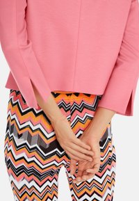 Haut rose ajusté avec fentes latérales et manches trois-quarts, associé à des leggings à motif zigzag multicolore en noir, blanc, rose et orange.
