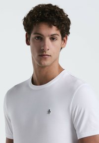 Witte katoenen t-shirt met een klassieke ronde halslijn en een klein zwart geborduurd pinguïnlogo op de linkerborst. Korte mouwen.