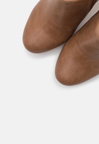 Hnědé kožené kotníkové boty s hladkým povrchem, špičatou špičkou a minimalistickým designem, se subtilním zrnem a bez viditelných kovových prvků.