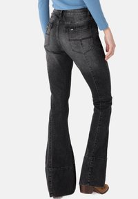 Black flared jeans with a faded texture. Features back pockets, contrasting seams, and a logo tag. Worn with brown heeled boots.