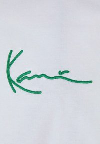 White fabric featuring green embroidered text that resembles a signature. The design is smooth with a lightweight texture.