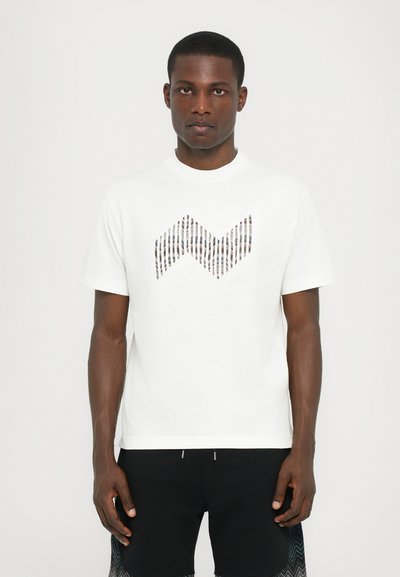 Hvid kortærmet t-shirt med et mønstret chevron-design i nuancer af brun og creme. Har en rund halsudskæring og en løs pasform.