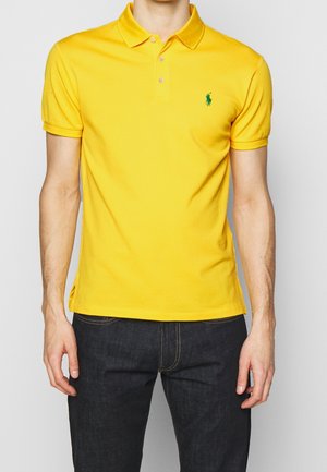 Yellow polo shirt made of cotton, featuring a three-button placket, short sleeves, and a small green embroidered logo on the chest.
